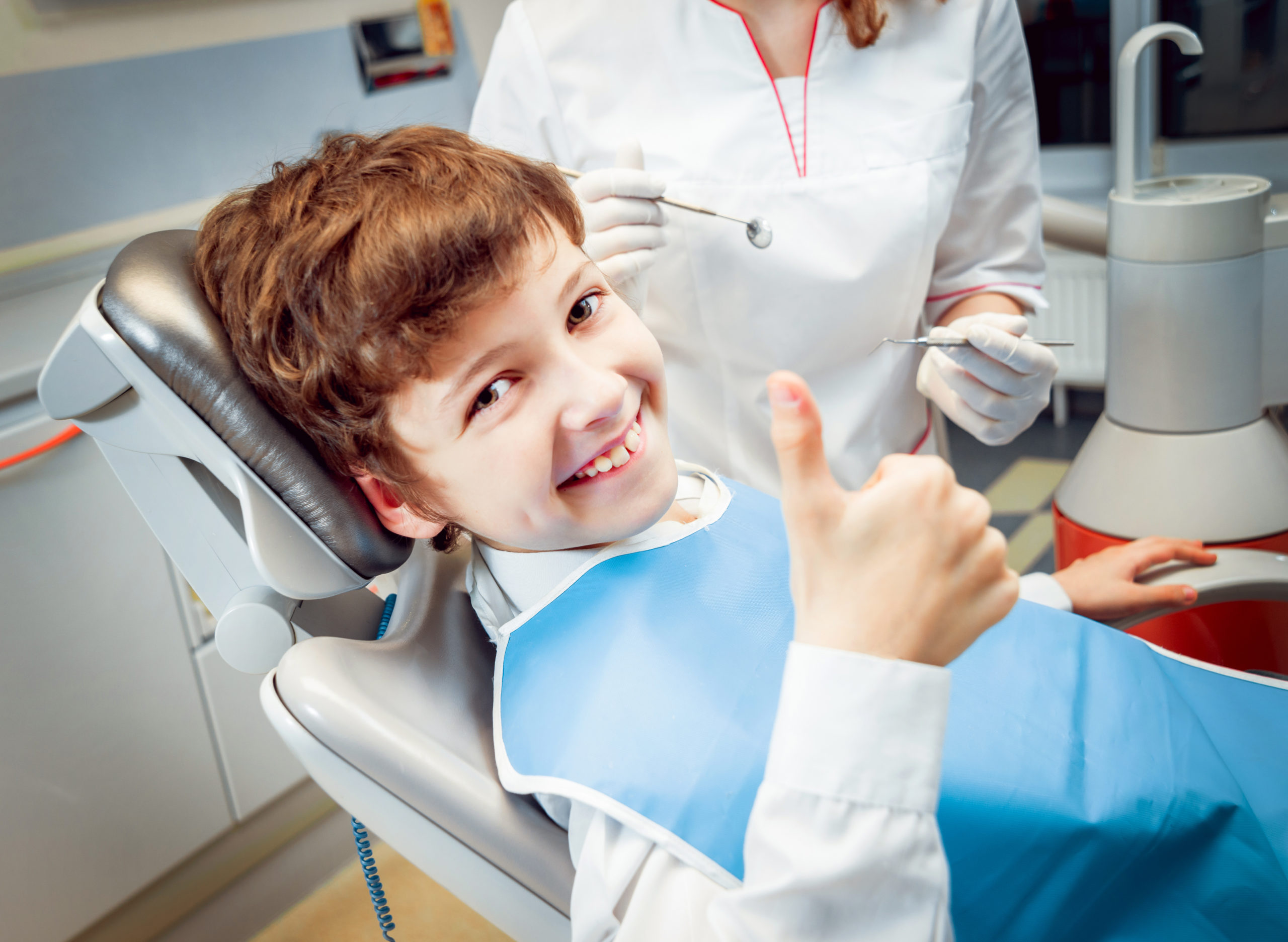 little boy in dentist's chair, smiling and showing a thumbs up