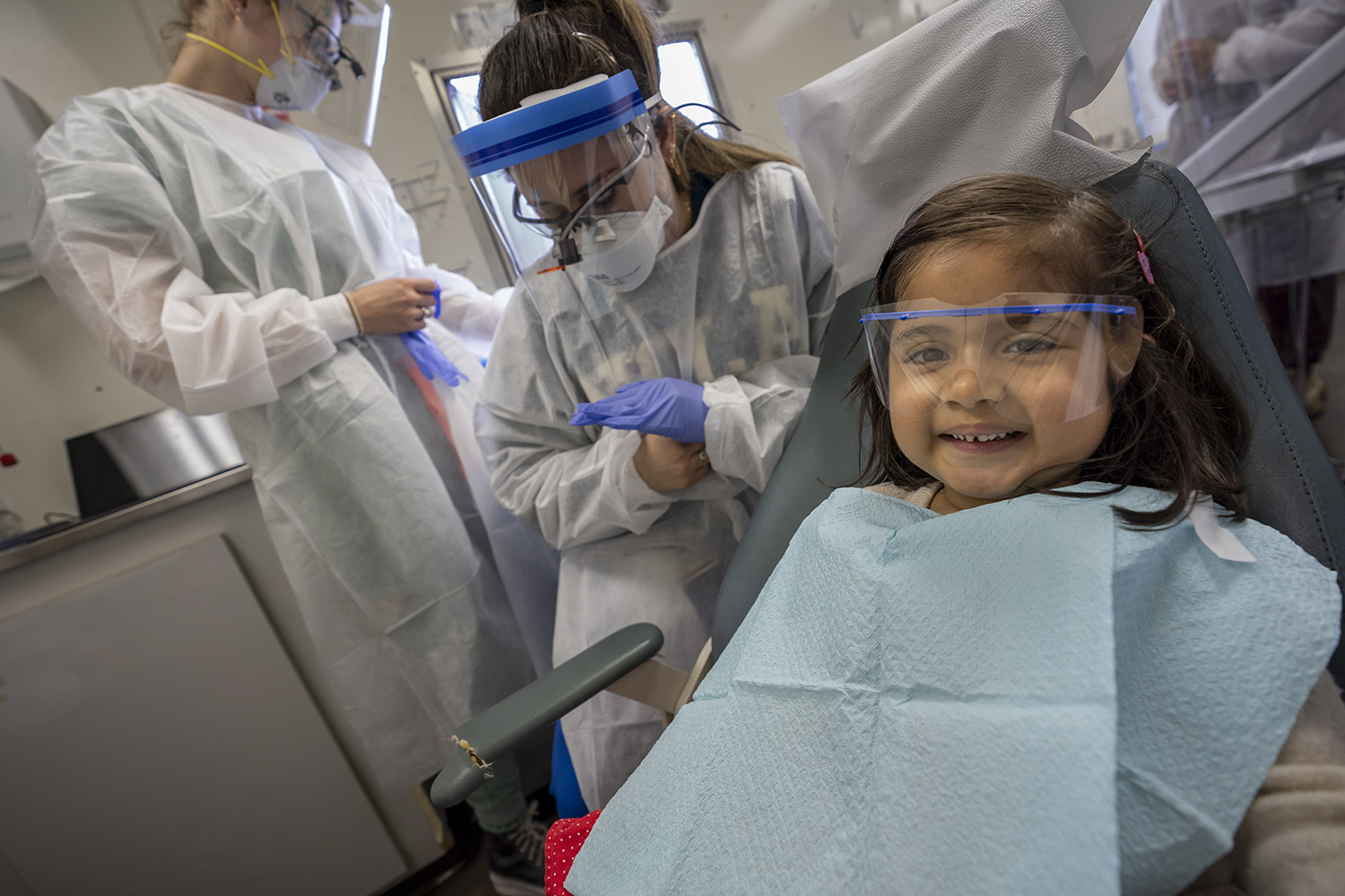 Little girl smiling in a mobile dental clinic with dental students behind her
