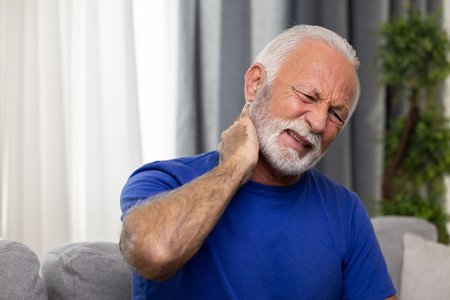 Elderly man with head and neck pain on sofa